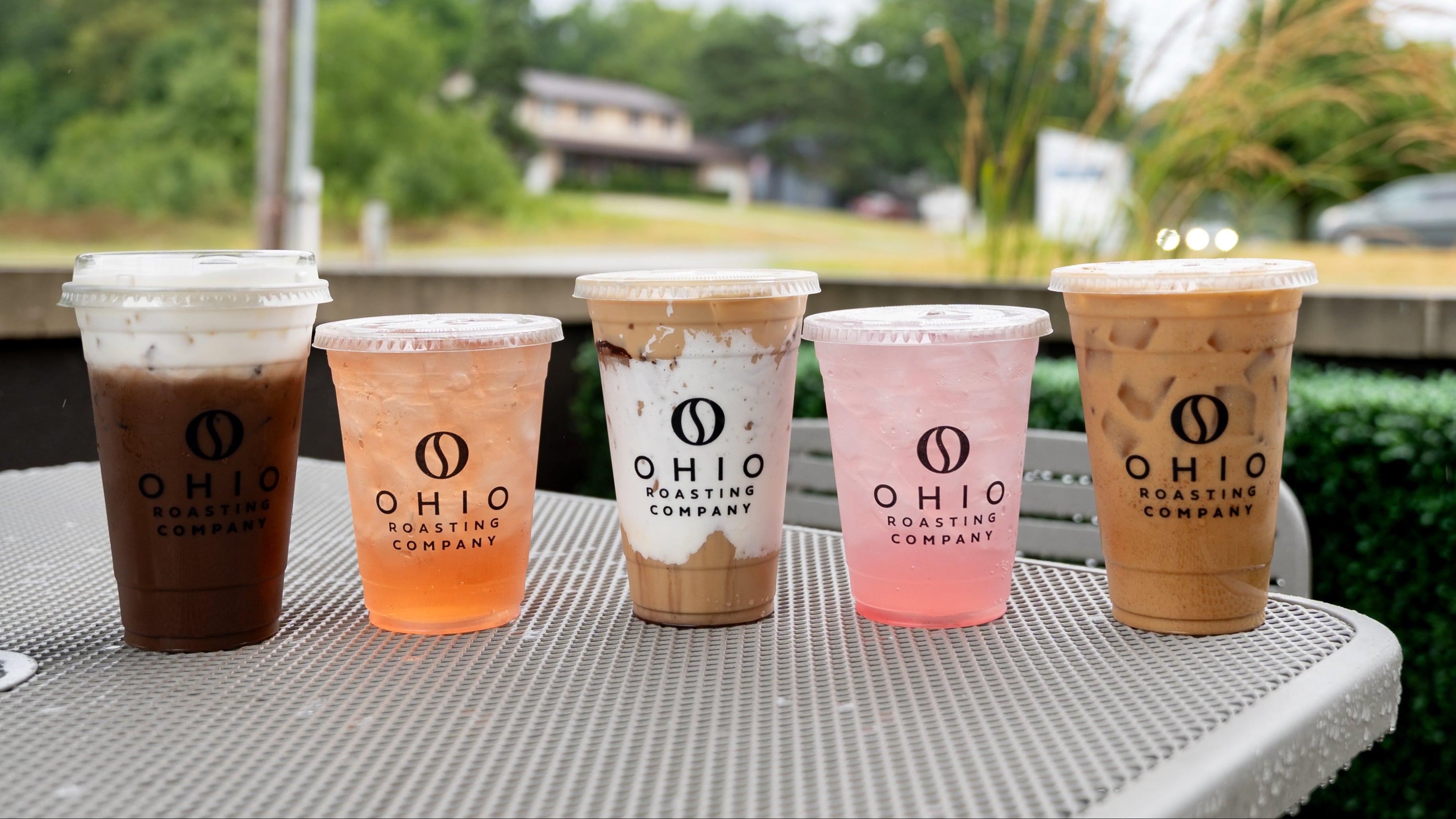 Five cups of iced coffee from Ohio Roasting Company on a metal table outdoors.